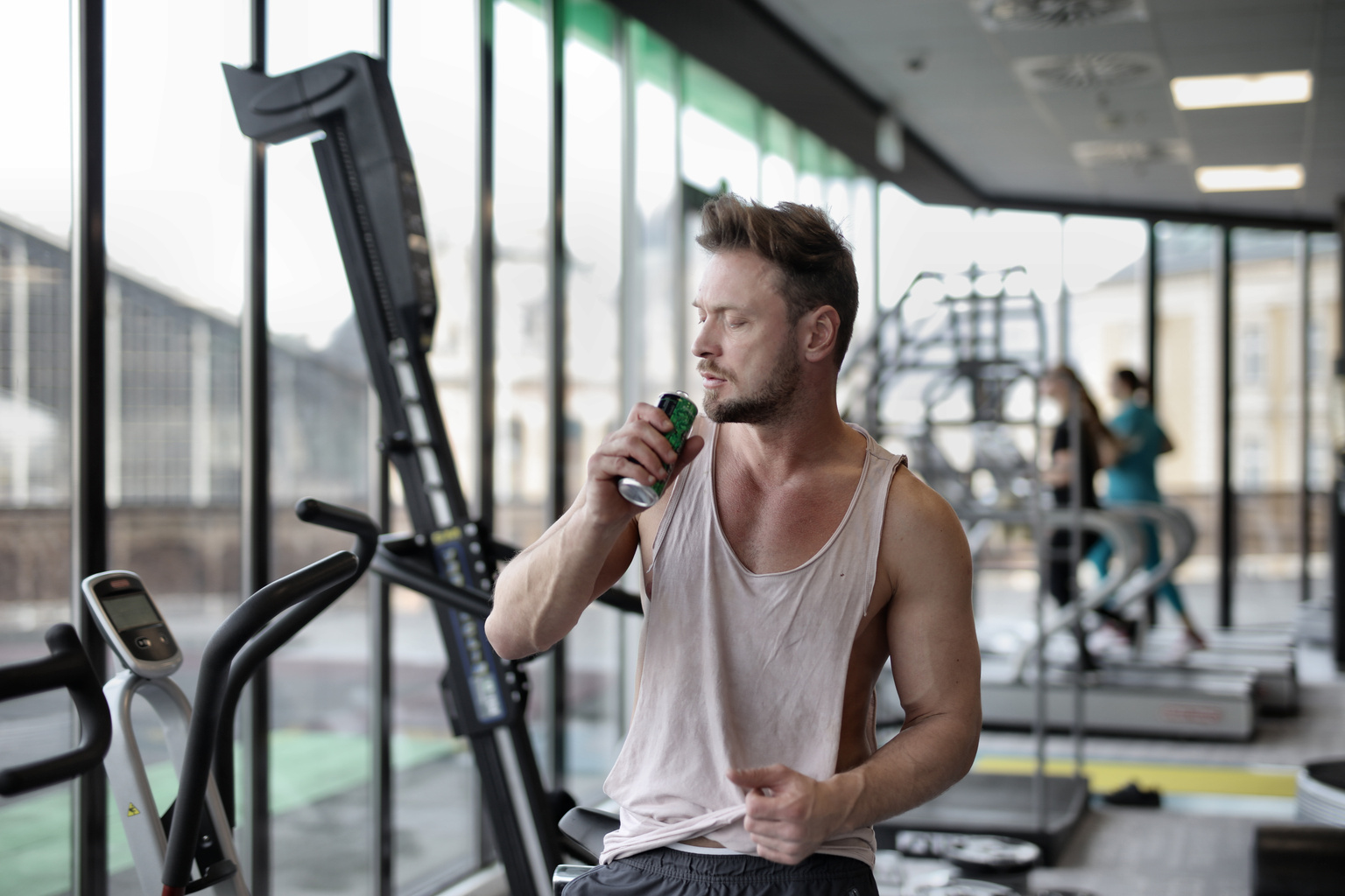 Strong young sportsman drinking energy drink during break in workout in modern gym